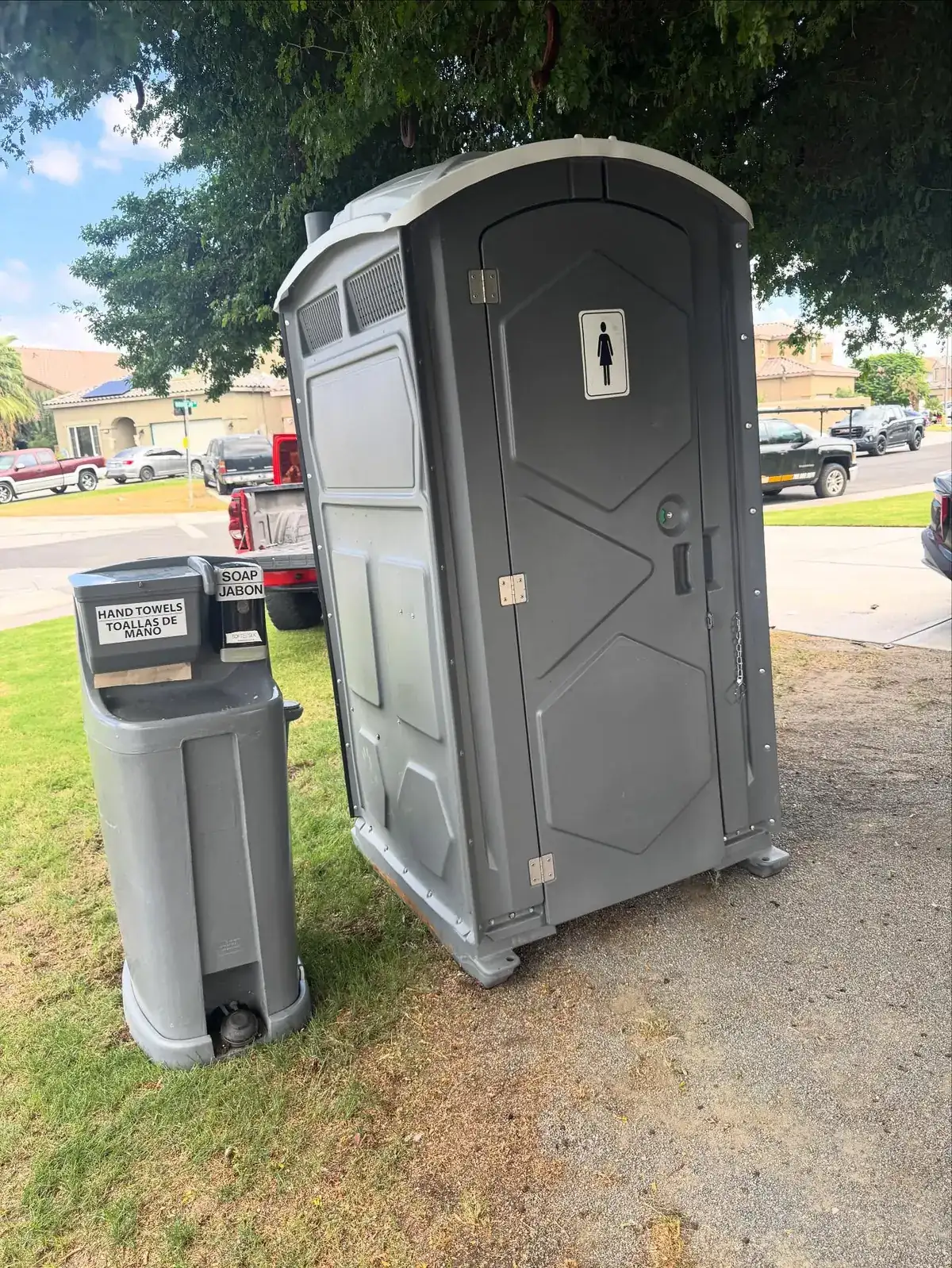 Portable toilet with a separate two-sided hand-wash sink station on a lawn