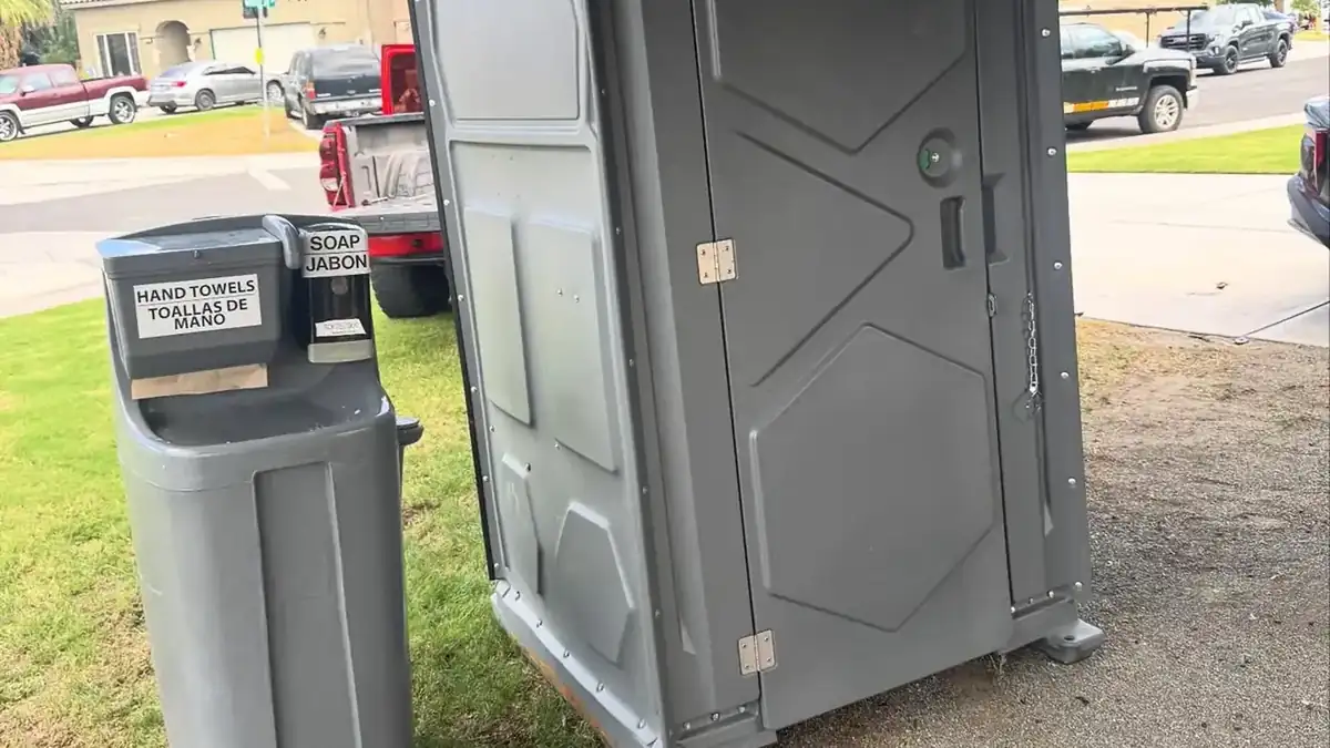 Two-sided hand-wash station beside a portable toilet on a lawn