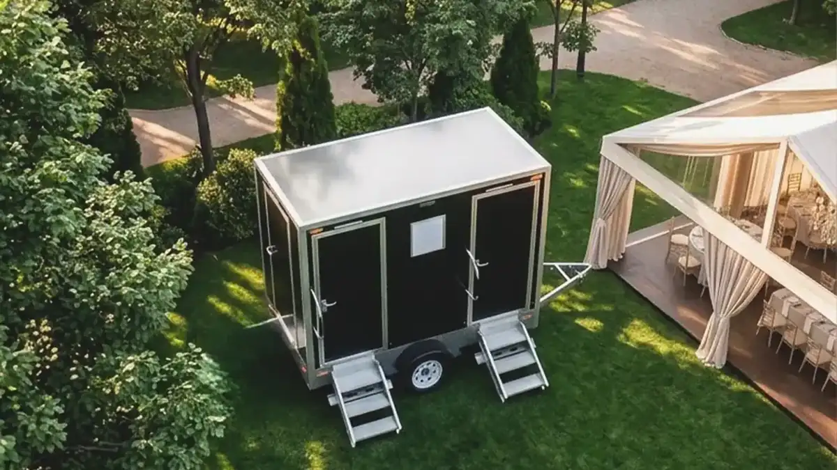 Restroom trailer parked on a lawn beside a wedding tent