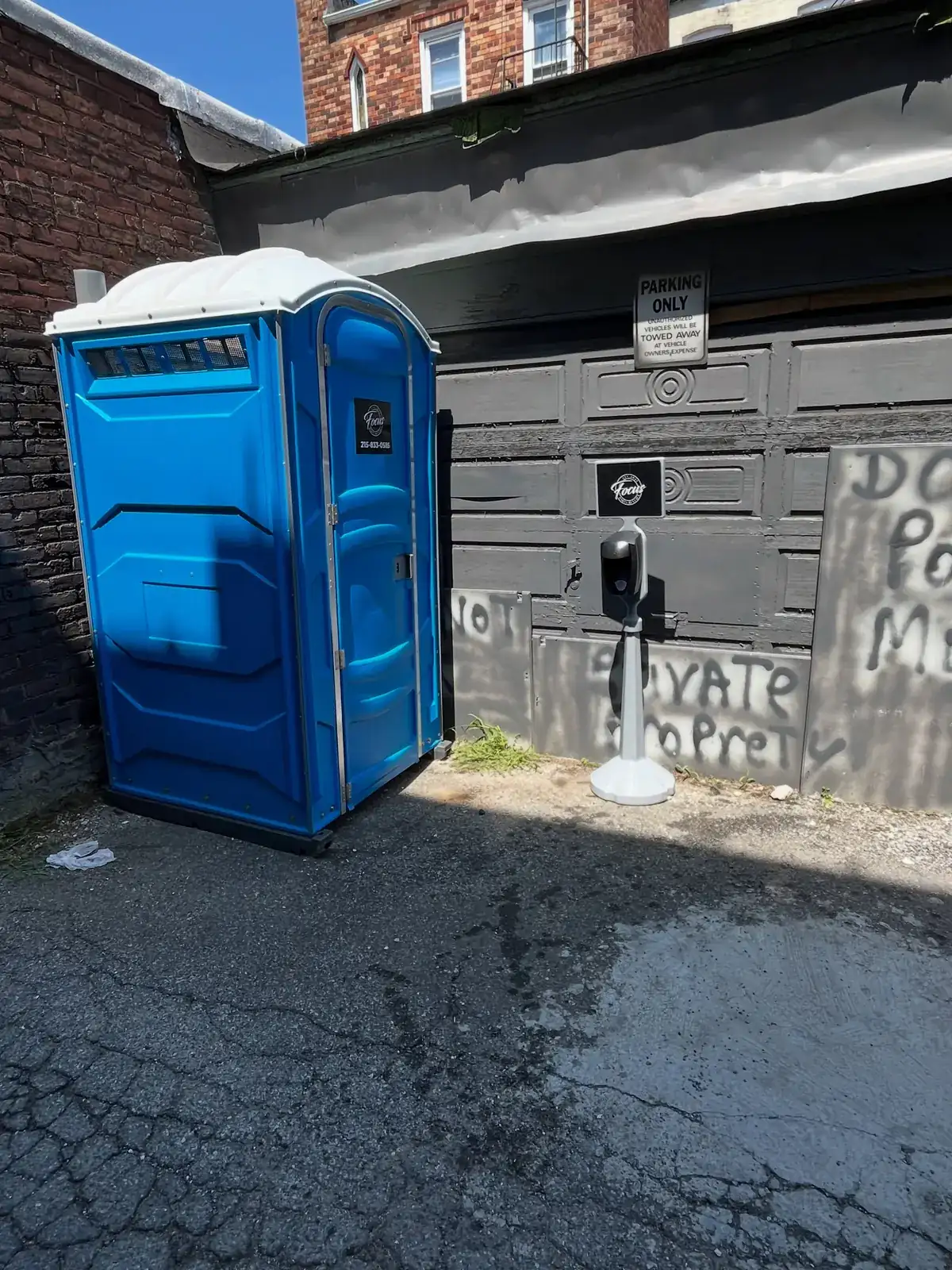 Standard portable toilet placed in a narrow side alley next to a building