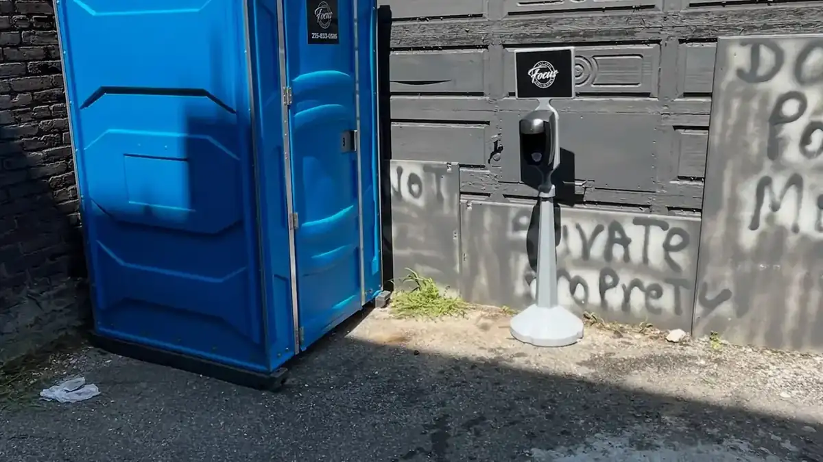 Standard porta potty placed on level pavement beside a building