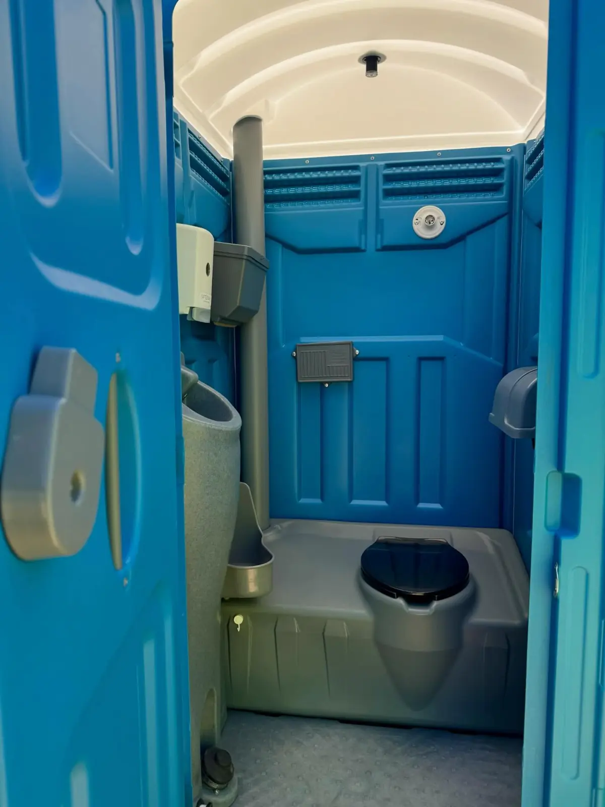 Inside a standard portable toilet showing the wall urinal next to the seat