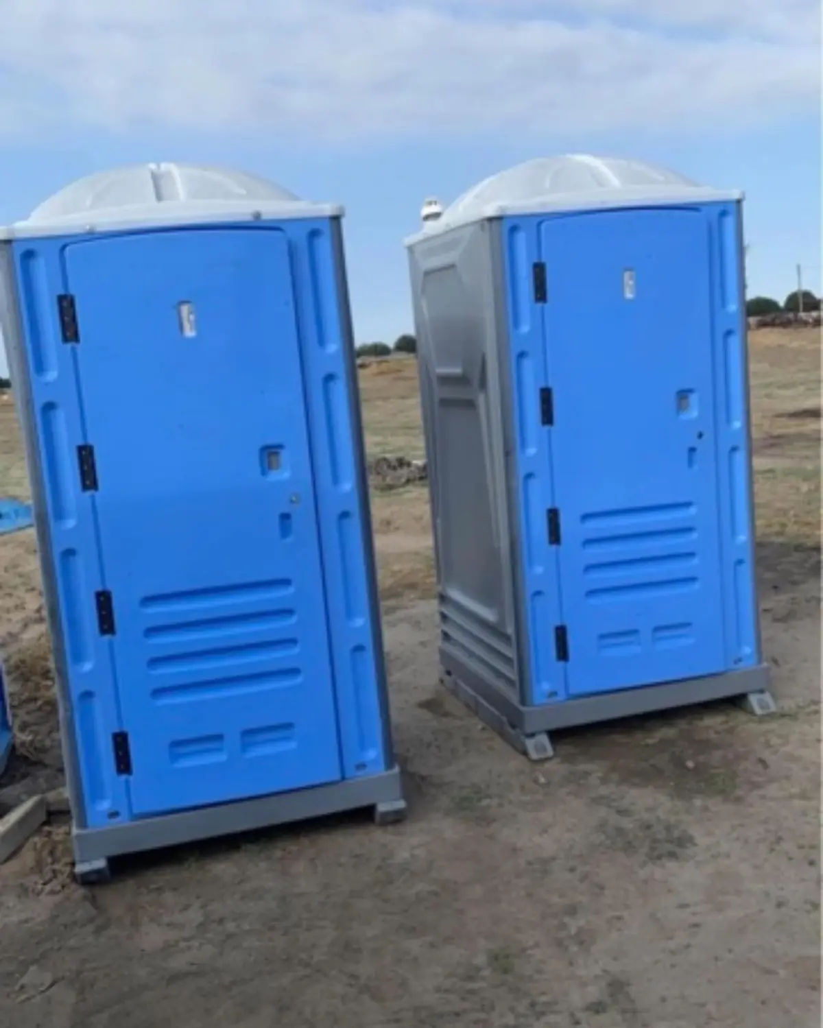 Two blue standard portable toilets set on level dirt at a work site