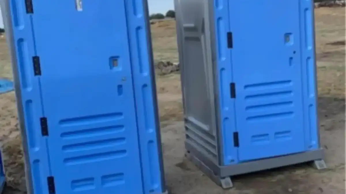 Two blue standard portable toilets set on level dirt at a work site