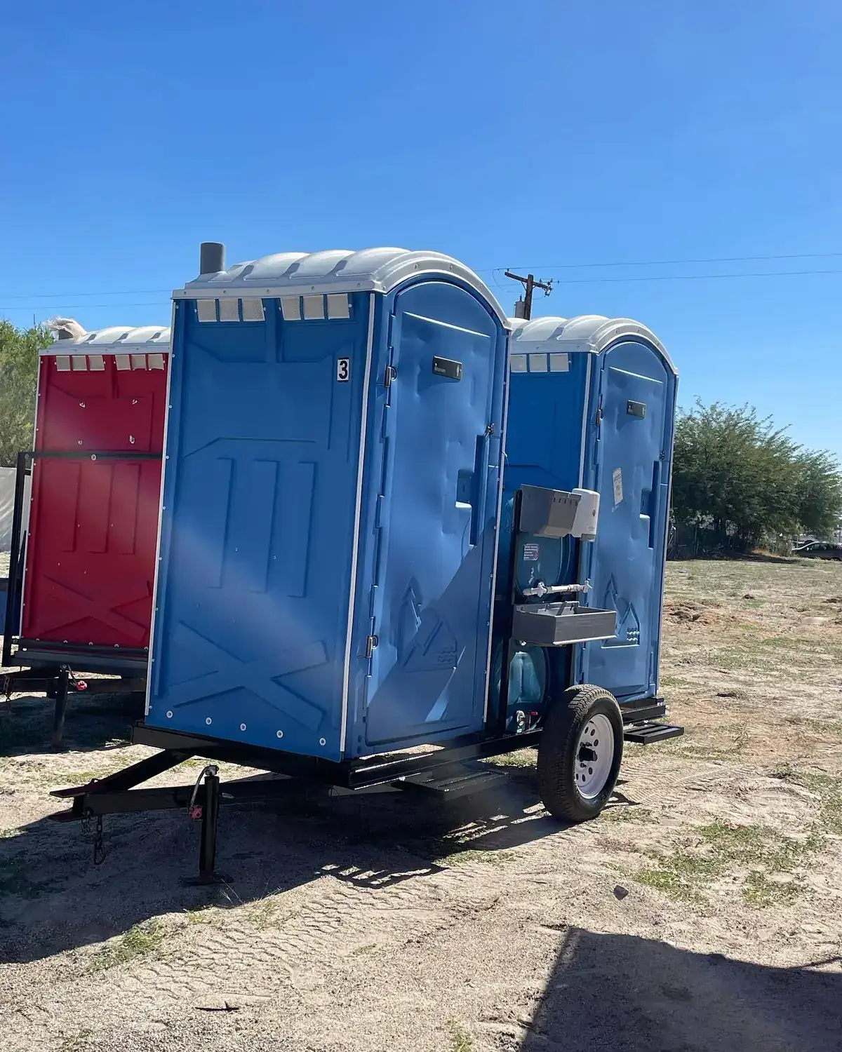 Trailer-mounted portable toilets parked on a gravel construction lot